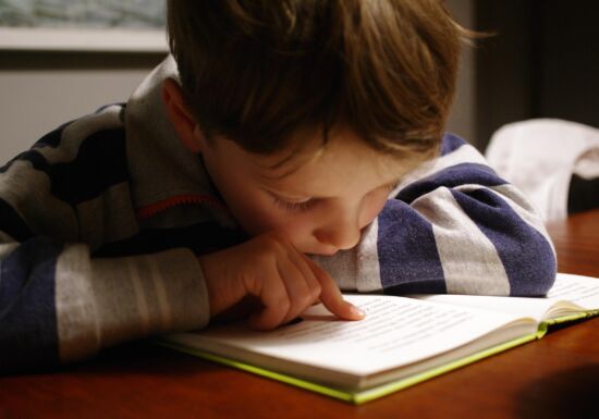 Jongetje met gestreepte trui leest een boek en volgt tekst met vinger