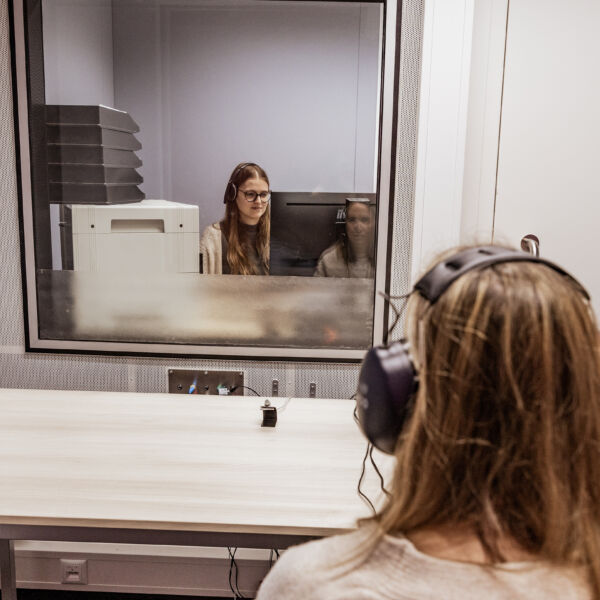 vrouwelijke audiologe doet gehoortest bij jonge vrouw in een audiocabine