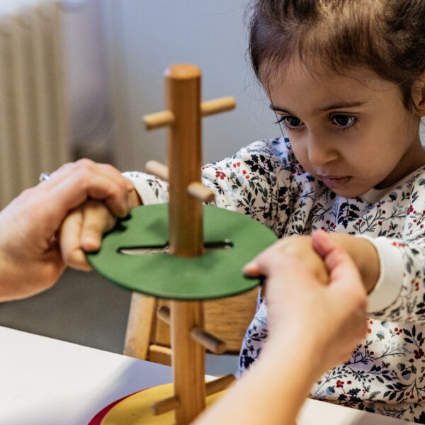Therapeute werkt met kind om groene houten schijf met onregelmatige vorm over een stok te schuiven