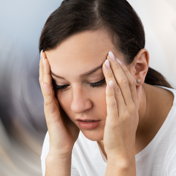 Vrouw met zwart haar en witte trui voelt zich duizelig. Ze heeft haar handen aan haar slapen en de achtergrond tolt.