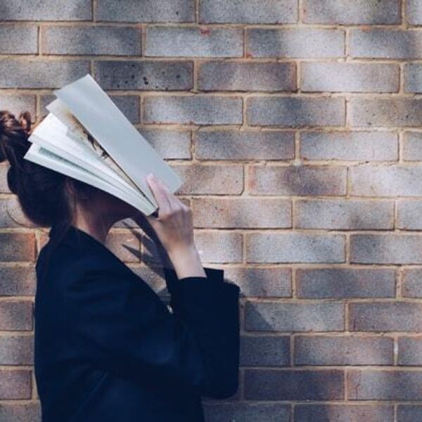 Studente staat voor bakstenen muur in profiel en slaat open cursusboek tegen haar gezicht