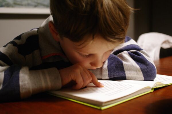 Jongetje met gestreepte trui leest een boek en volgt tekst met vinger